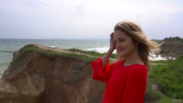 Счастливая молодая женщина в красном платье веселится и гуляет по скале морского побережья
 - Кадры, видео