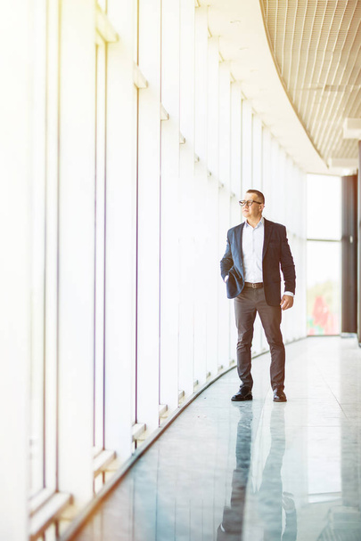 full length picture of a mid aged business man walking towards the camera and smiling in office building - Fotoğraf, Görsel