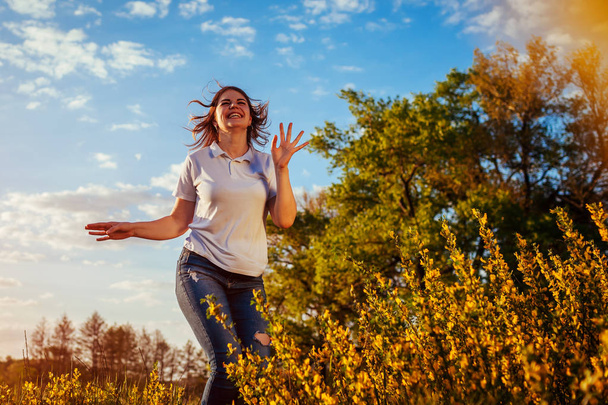 Jonge vrouw springen, uitgevoerd en plezier in voorjaar veld bij zonsondergang. Gelukkig en vrij meisje ontspant en geniet van de natuur - Foto, afbeelding