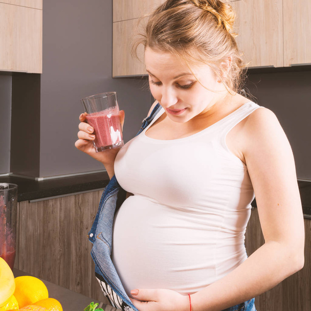 Pregnant woman makes a fruit smoothie for herself and her child in the kitchen - 写真・画像
