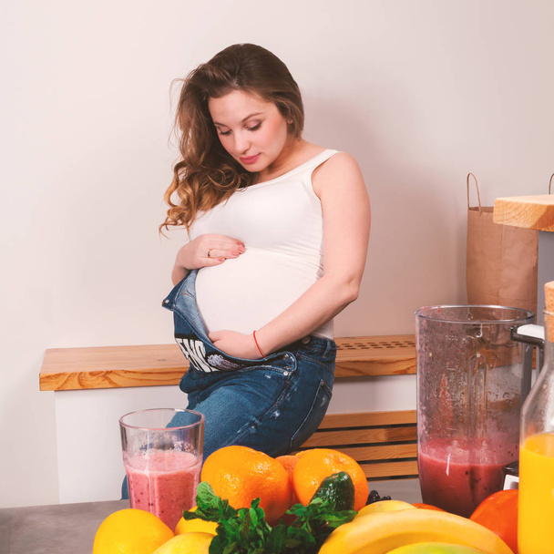 Beautiful pregnant woman stroking her stomach with fruits in the foreground - Foto, afbeelding