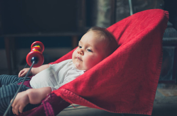 A little baby is sitting in a bouncy chair by the window - Foto, immagini
