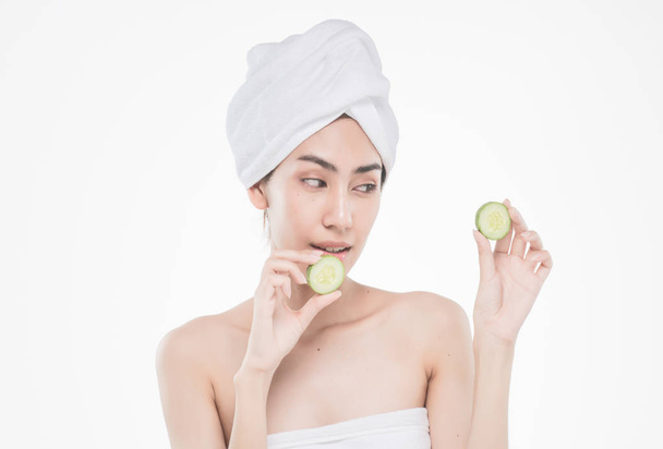 beautiful asia woman with towel on head with perfect clean skin smiling holding cucumber slices over white background. Beauty cosmetology and spa. - Foto, Imagem