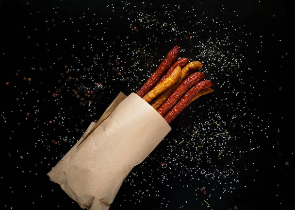 Smoked sausages on a paper texture on a dark background with pepper and large salt, free space for text, daylight - Photo, Image
