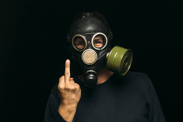 Mann mit Gasmaske zeigt Mittelfinger auf dunklem Hintergrund - Foto, Bild