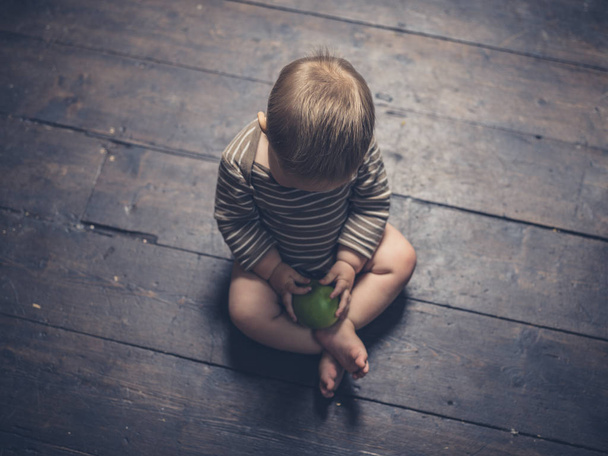 Little baby sitting on floorboards with apple - Photo, Image