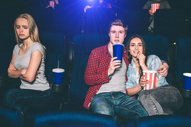 Beautiful couple is sitting together and watching movie. Brunette girl is eating popcorn and guy is drinking coke. She is offended of being alone. - Fotografie, Obrázek