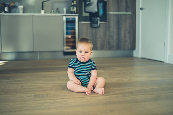 Little baby sitting on the floor in kitchen - Фото, изображение