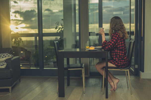 Woman having breakfast by window in city apartment - Photo, Image