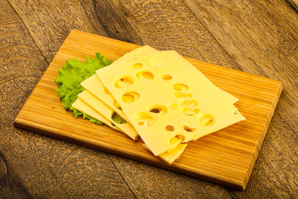 Sliced cheese with salad leaves over the wooden background - Photo, Image