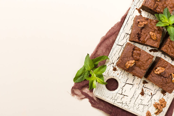 Brownie sweet chocolate dessert with walnuts and meant leaves on retro board with copy space on pastel beige background. - Φωτογραφία, εικόνα