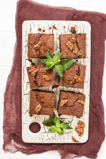 Postre de chocolate dulce Brownie con nueces y hojas significadas en tablero retro con espacio de copia sobre fondo beige pastel
. - Foto, Imagen