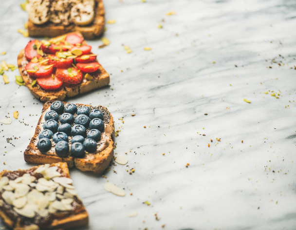 Healthy breakfast or snack. Vegan whole grain toasts with fruit, seeds, nuts and peanut butter over marble background - Photo, Image