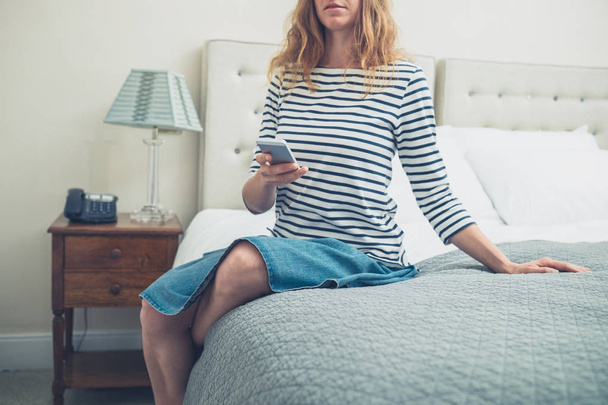 Woman on bed in hotel room using smart phone - Foto, afbeelding