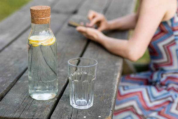 A bottle of water with lemon and a glass. A table and a person w - Foto, imagen