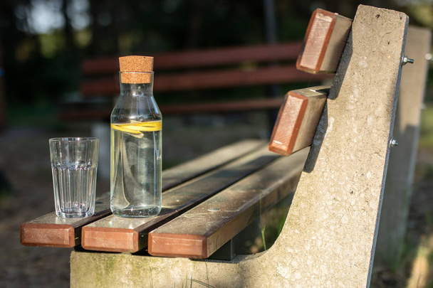 A bottle of water with lemon and a glass. A bench on which a ref - Zdjęcie, obraz