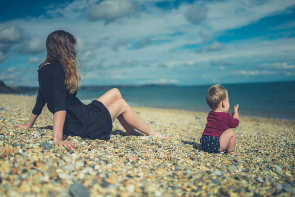 Young mother sitting on beach with her baby - Фото, зображення