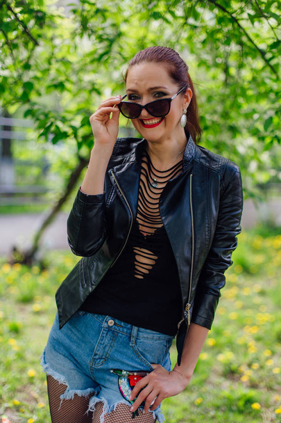 Charming woman dressed in a leather jacket near bird-cherry tree - Zdjęcie, obraz