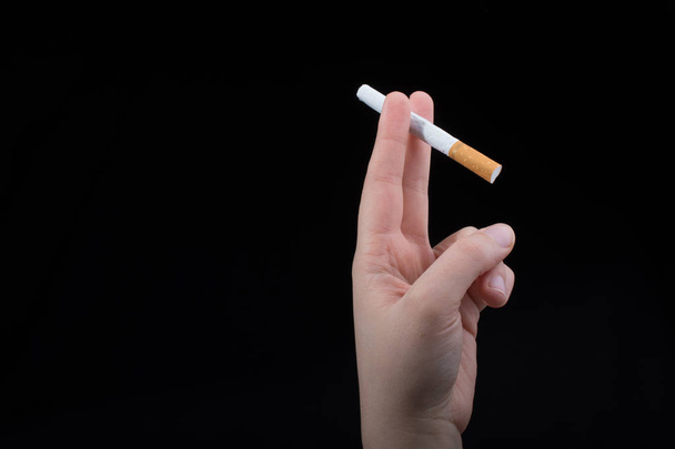 La mano sostiene un cigarrillo sobre fondo negro - Foto, Imagen
