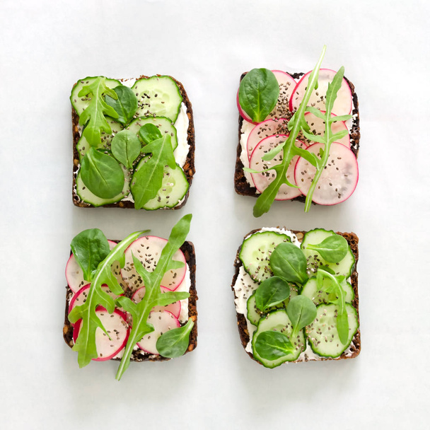 Sandwiches with cream cheese, fresh cucumber, radish, chia seeds and arugula on white paper - Fotografie, Obrázek
