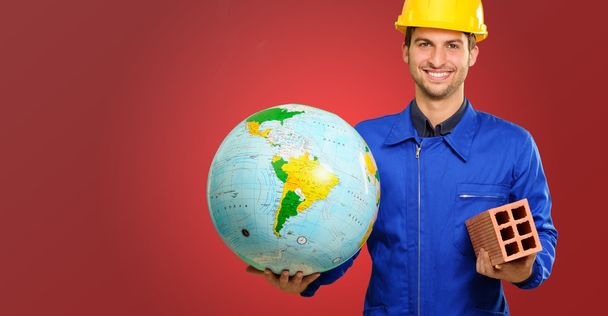 Gelukkig jonge bouwvakker holding globe en bakstenen - Foto, afbeelding