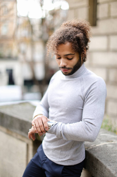 Black male person looking at watch and wearing grey turtleneck sweater. - Photo, Image
