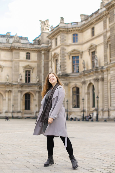 Szép nő, szürke kabátot áll közel a párizsi Louvre-ban. - Fotó, kép