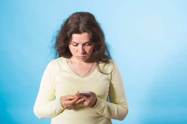 Portrait of a woman sending text message from her phone over blue background - Fotografie, Obrázek