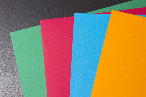Multi-colored sheets of paper on a black background. Sheets of paper of different colors. colored sheets are spread out in a fan - Fotografie, Obrázek