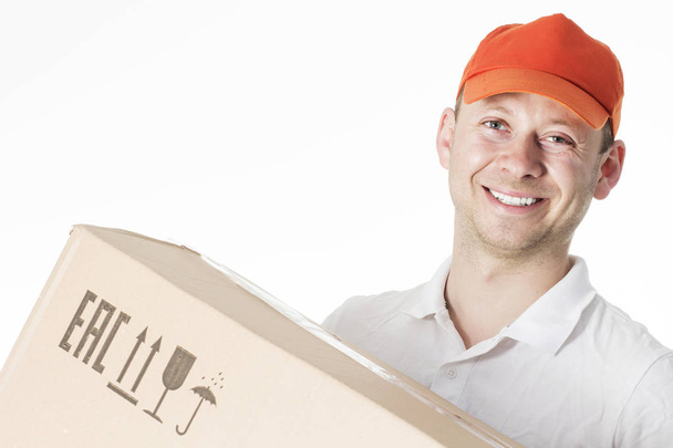 Portrait of smiling male courier in orange cap with cardboard box in hands isolated on white background. Delivery courier concept - Photo, image