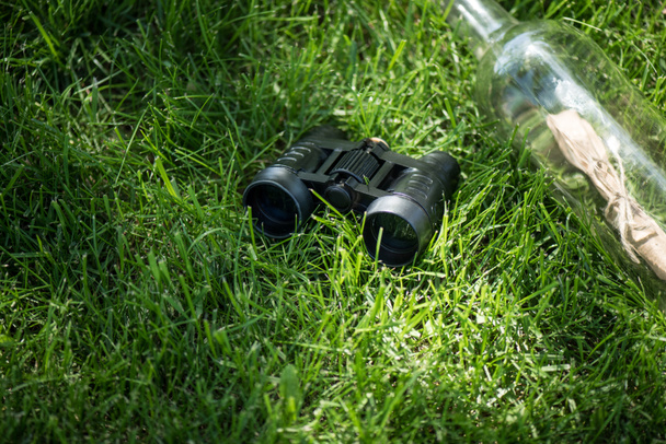 close up view of binoculars and paper in glass bottle arranged on green lawn - Photo, Image