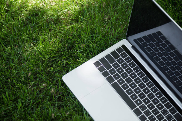 закрытый вид на открытый ноутбук с экраном на зеленой траве
 - Фото, изображение