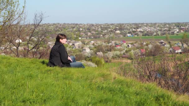 Een jonge vrouw ligt op een heuvel en kijkt neer op het huis. Concept: terugkeer naar huis - Video
