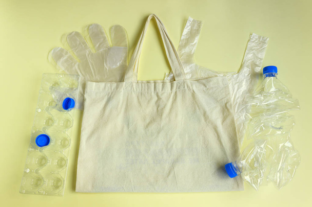 Sur le sac réutilisable en tissu reposent des sacs jetables en cellophane, des gants, un récipient de stockage des œufs, des bouteilles en plastique froissées. Concept de recyclage
  - Photo, image