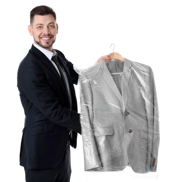 Young businessman holding hanger with jacket in plastic bag on white background. Dry-cleaning service - Valokuva, kuva