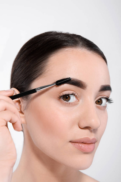 Beautiful woman with perfect eyebrows applying makeup on light background - Valokuva, kuva