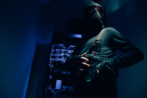низький кут зору хакер в чорний одяг і окуляри з різних кабелі на тлі - Фото, зображення