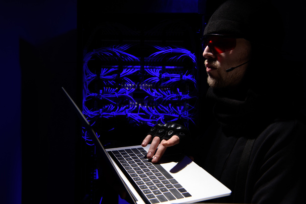 vista lateral de hacker en gafas usando portátil con cables en el fondo
 - Foto, imagen