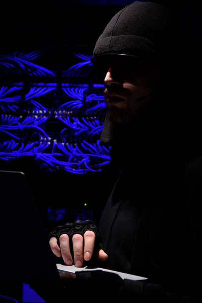 вид збоку хакер в окулярів, використовуючи ноутбук з кабелі на тлі - Фото, зображення