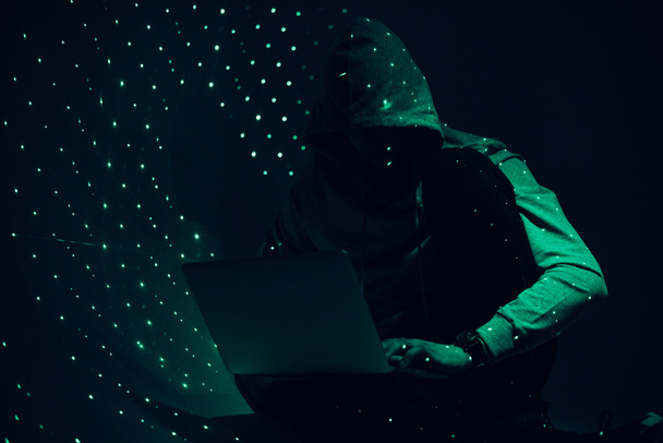 toned picture of silhouette of hacker in hoodie using laptop - Foto, imagen