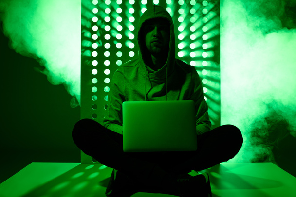 imagen tonificada de hacker masculino con capucha con portátil
 - Foto, imagen