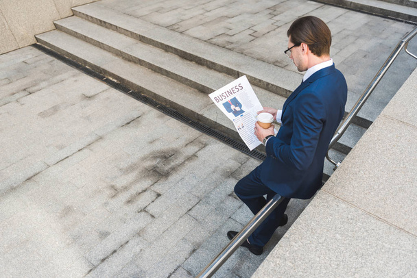 high angle view of young businessman with coffee to go reading newspaper - Photo, image