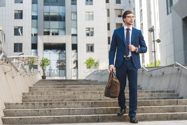 handsome young businessman in stylish suit with briefcase in business district - Photo, Image