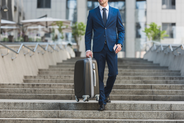 cropped shot of businessman with luggage and flight tickets going down stairs in business district - Fotografie, Obrázek