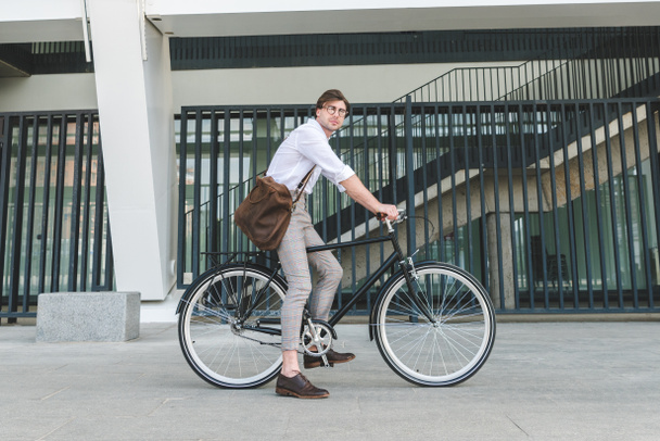 side view of attractive young man riding vintage bicycle on city street - Фото, зображення