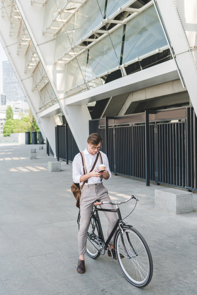 jovem bonito com café para ir usando smartphone enquanto sentado na bicicleta
 - Foto, Imagem