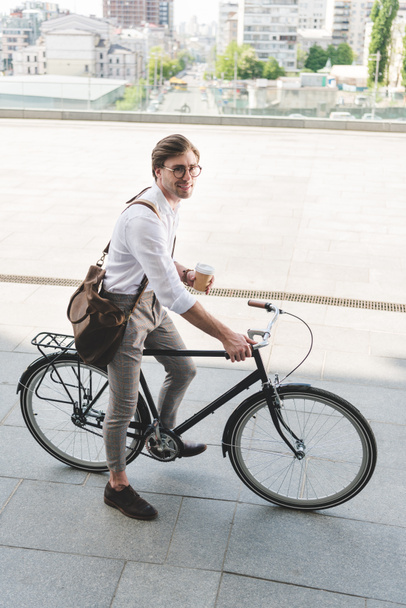 high angle view of attractive young man with paper cup of coffee on vintage bicycle - 写真・画像