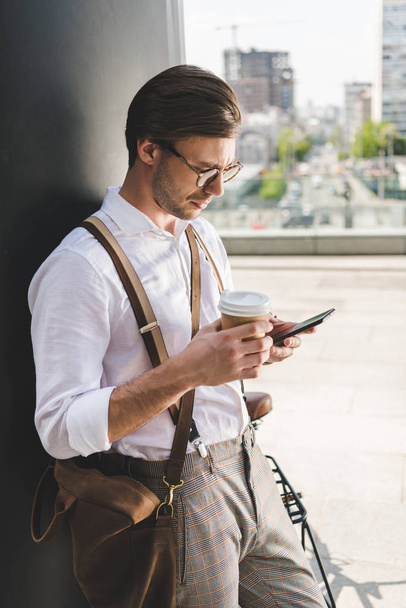 stylish young man with paper cup of coffee to go using smartphone - Foto, imagen