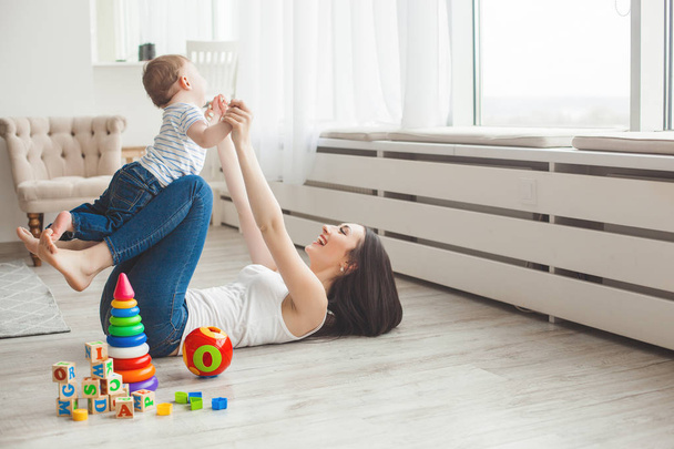 Young pretty mother playing with her little son. Cheerful family having fun indoors with little baby son - Fotoğraf, Görsel