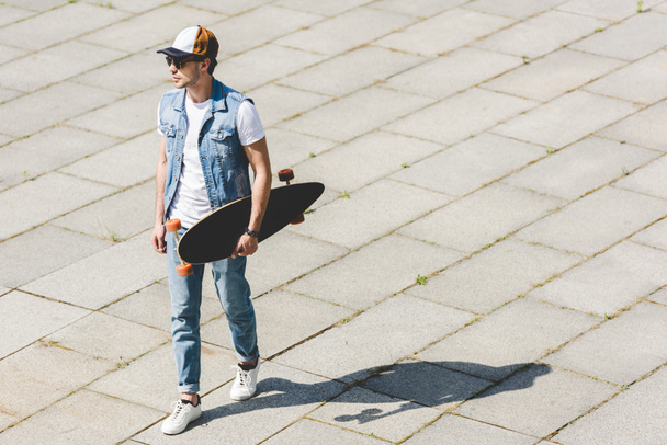 yakışıklı genç adamın elinde kaykay ile yürüme yüksek açılı görünüş - Fotoğraf, Görsel